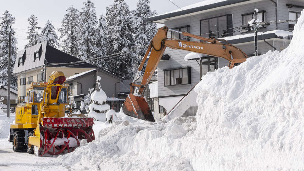 Snow plows clearing large amounts of snow in front of houses
